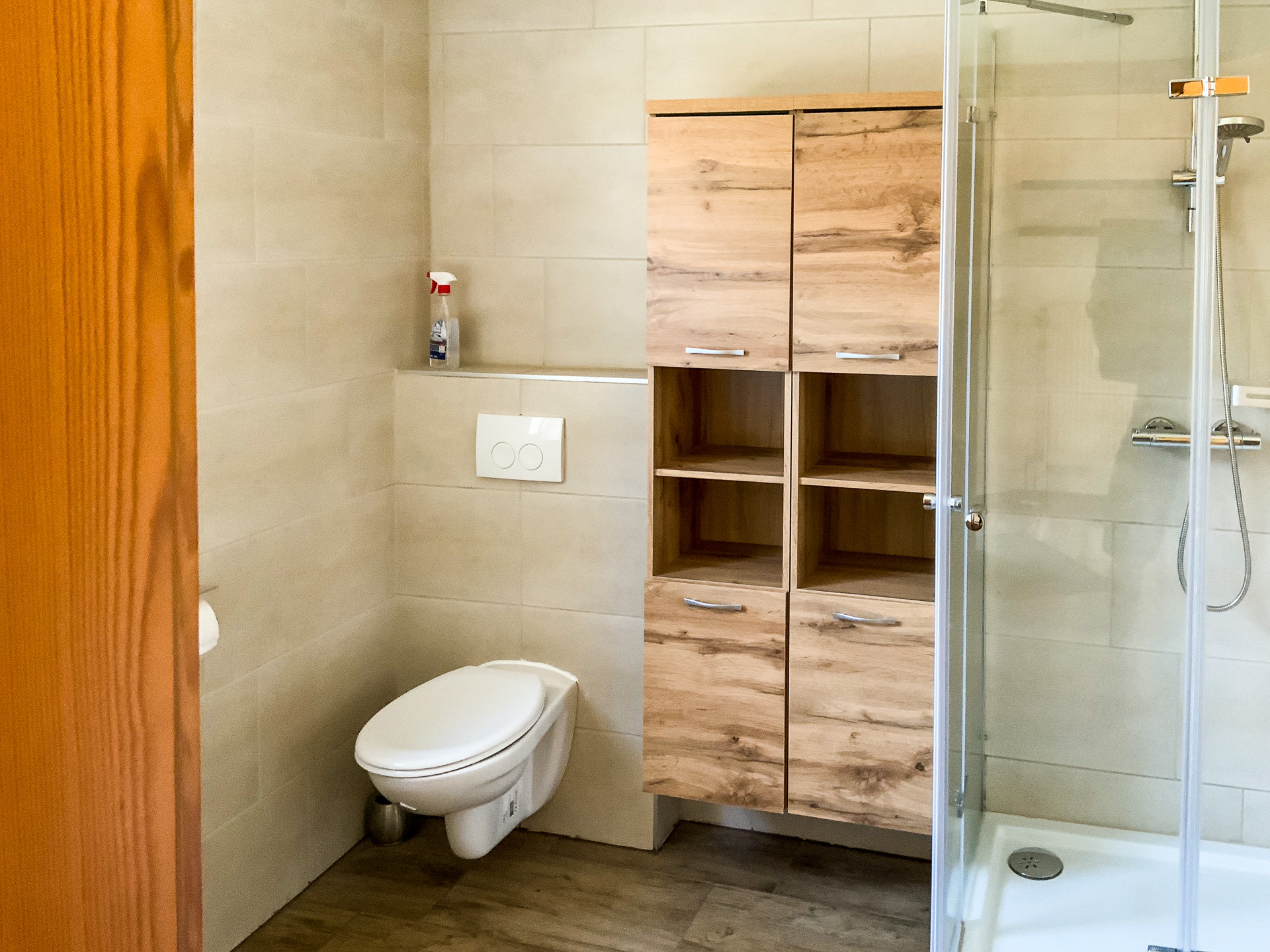 Dieses stilvolle Badezimmer bietet alles für einen angenehmen Aufenthalt. Die moderne Dusche sorgt für Komfort, während praktische Holzschränke genügend Stauraum bieten. Helle Fliesen und eine moderne Ausstattung schaffen eine freundliche Atmosphäre. Perfekt für entspannte Momente in Ihrer Ferienwohnung!