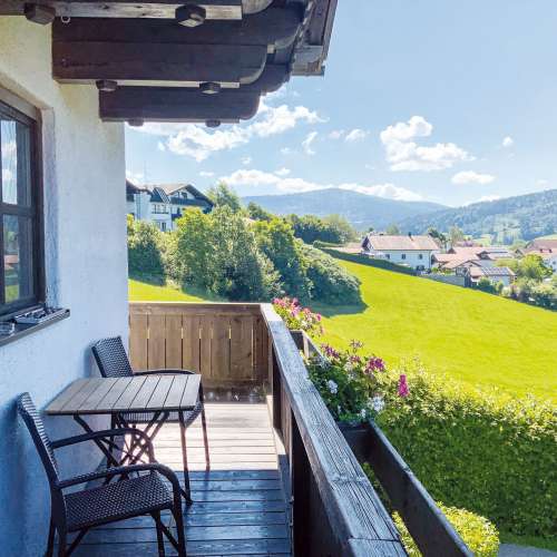 Genießen Sie entspannte Stunden auf dem sonnigen Balkon Ihrer Ferienwohnung. Der gemütliche Sitzbereich lädt zum Verweilen ein, während Sie die herrliche Aussicht auf grüne Wiesen, idyllische Häuser und die beeindruckende Berglandschaft genießen.